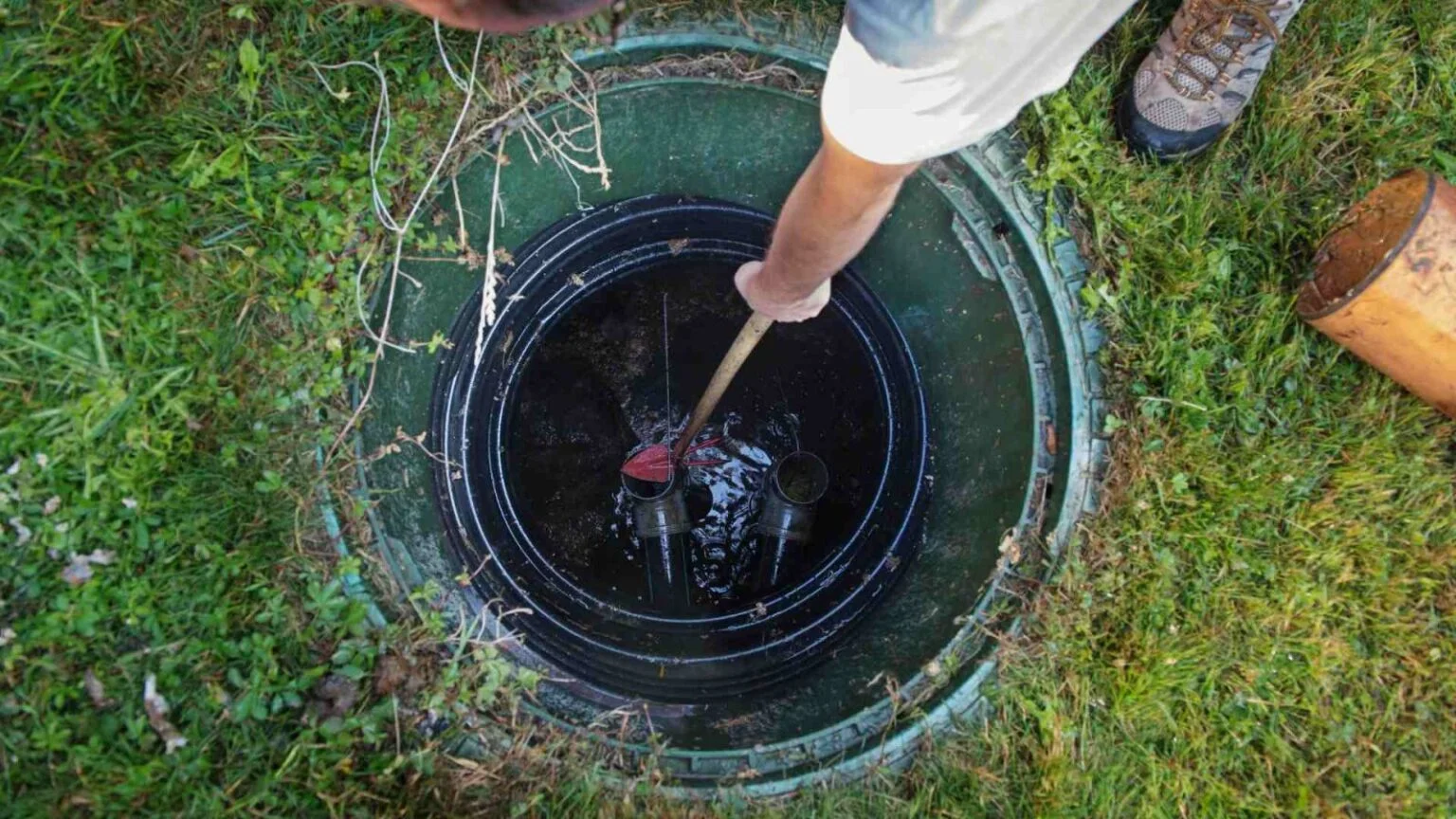Technician checking sludge levels inside an open septic tank lid during maintenance in Kannapolis, NC