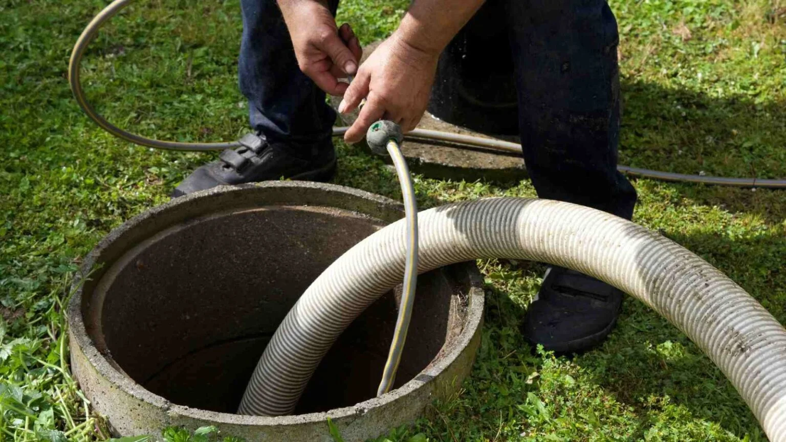 Pumping hose lowered into a concrete septic tank lid opening during a pump-out