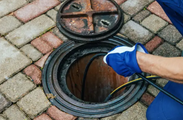 Technician feeding a hydro jetting hose into an open drain access on brick paving